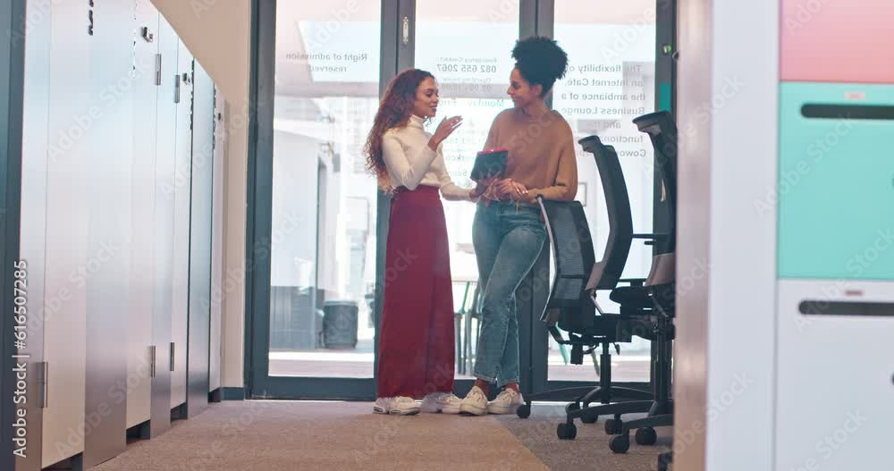Wide shot of two women standing discussing work in open plan office, full length Wide shot of two women standing discussing work in open plan office, full length