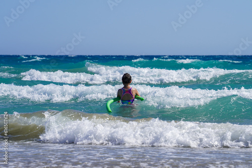 Girl swims with green foam swimming tube near beach of wavy mediterranean sea