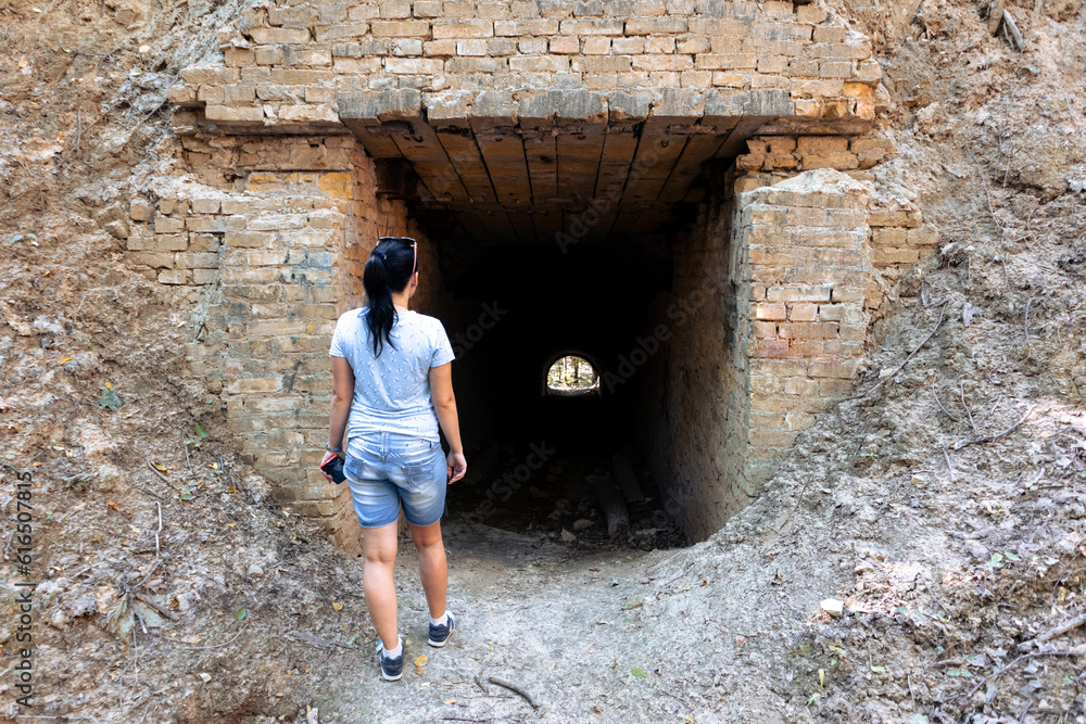 A woman stands next to the entrance to an old underground tunnel through a large hill