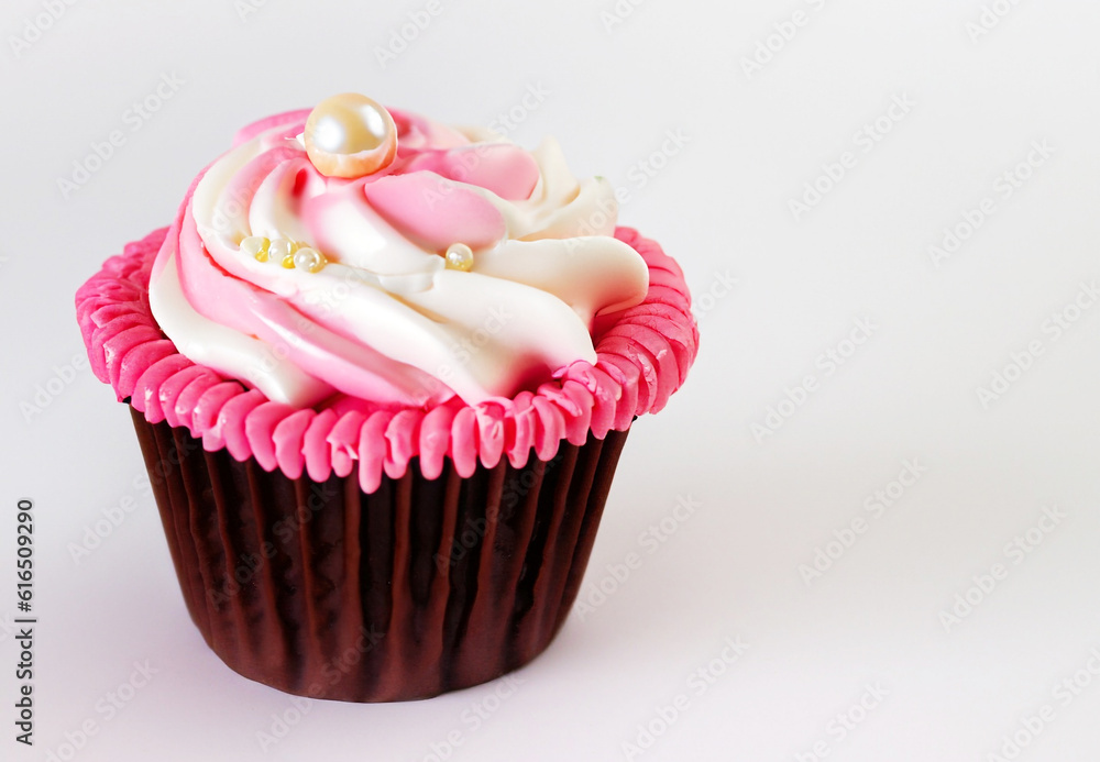 A pink cupcake with white frosting and a pearl accent on white background A pink cupcake with white frosting and a pearl accent on white background