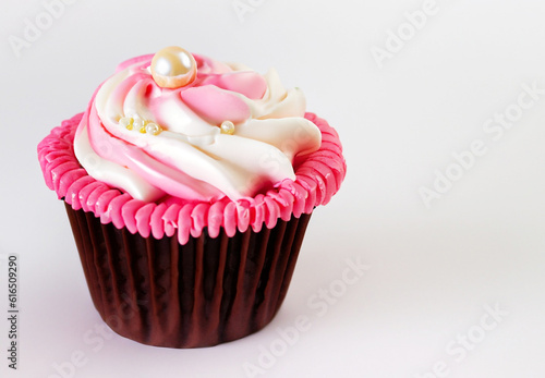 A pink cupcake with white frosting and a pearl accent on white background