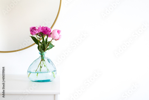 Pink peonies in the apartment. Home decoration  pink peonies on table in white room. Vase with beautiful peony flowers on table in bedroom. Flowers in a vase at home. Mirror reflection  gold frame