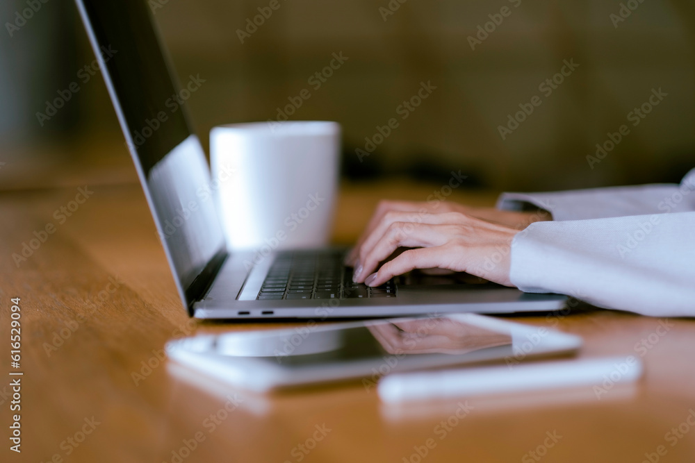 Crop Asian beautiful woman hands typing at laptop on desk with blur tablet, digital pen and a cup of coffee and copy space. Crop Asian beautiful woman hands typing at laptop on desk with blur tablet, digital pen and a cup of coffee and copy space.