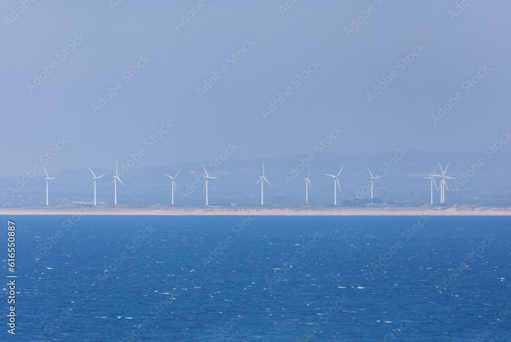 Obraz premium View of Wind turbines generating green renewable energy with Atlantic Ocean in foreground. Wexford, Ireland
