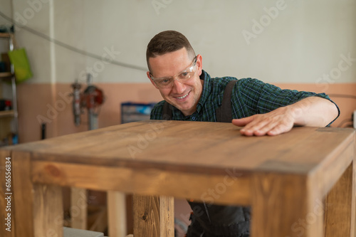 Male carpenter finishing work on wooden table in workshop.  © Михаил Решетников