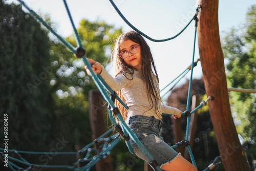 Portrait of a beautiful caucasian girl stands half-side on a rope swing in a park on a playground