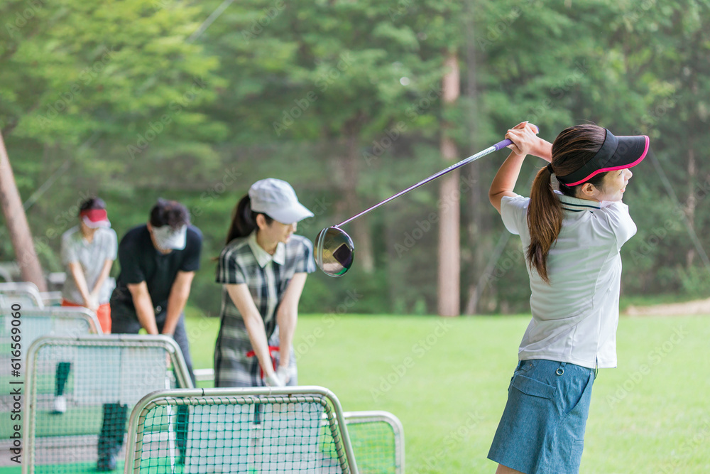 Obraz premium ゴルフ練習場・打ちっぱなし・ゴルフセンターでスイングの練習するゴルフ選手・ゴルファーの男女 