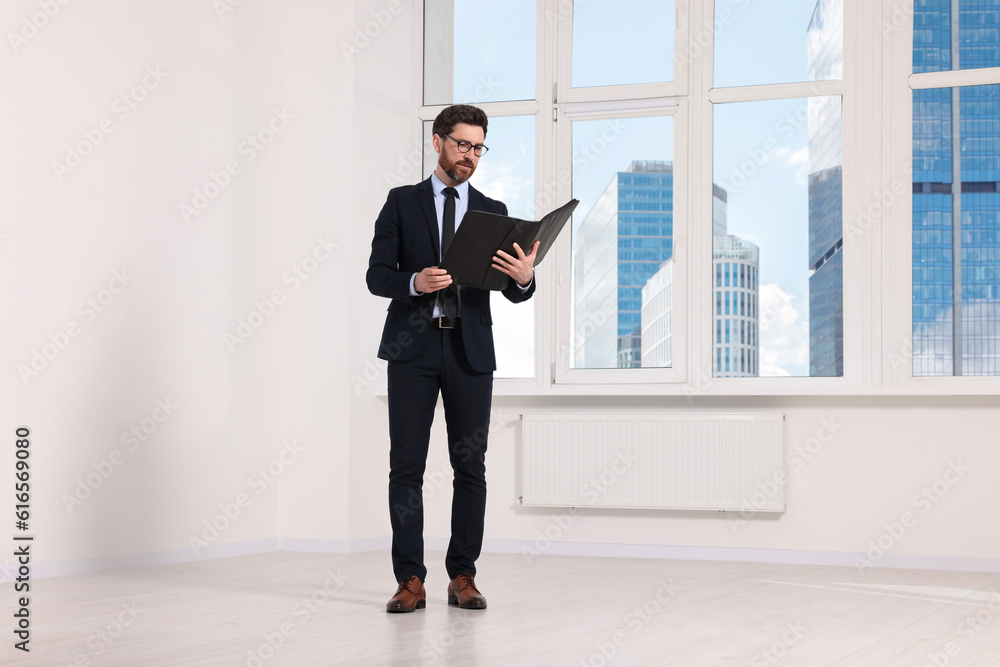 Handsome real estate agent with documents in empty room, space for text Handsome real estate agent with documents in empty room, space for text