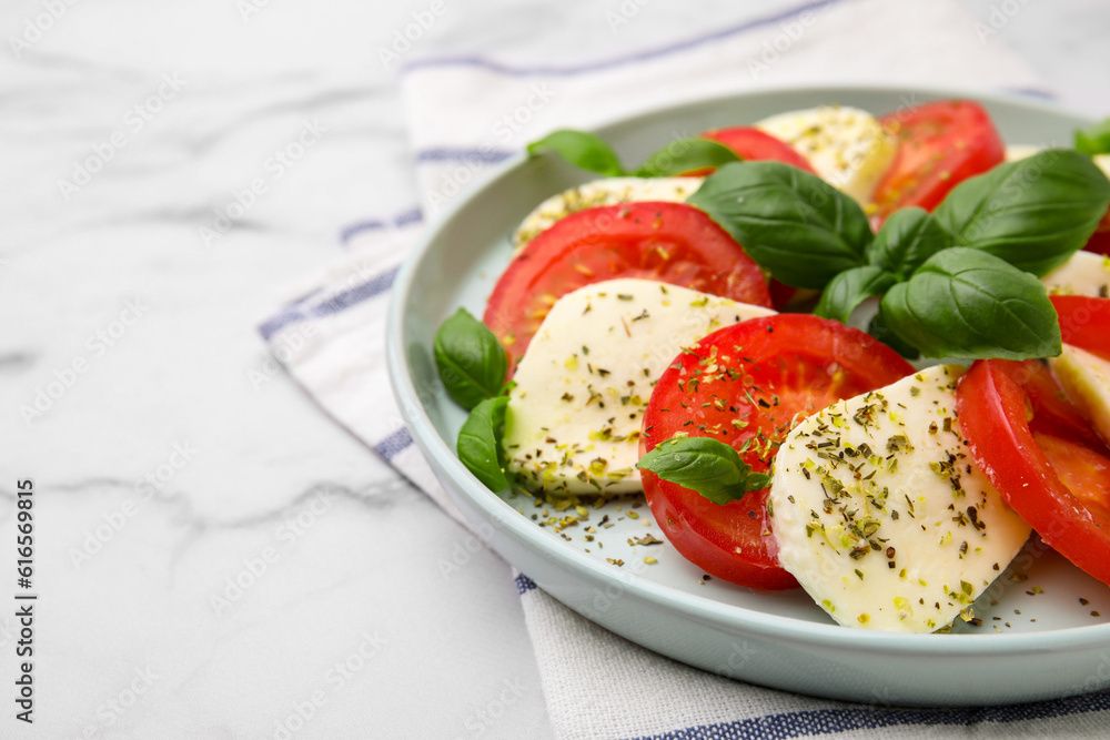 Caprese salad with tomatoes, mozzarella, basil and spices on white marble table, closeup. Space for text