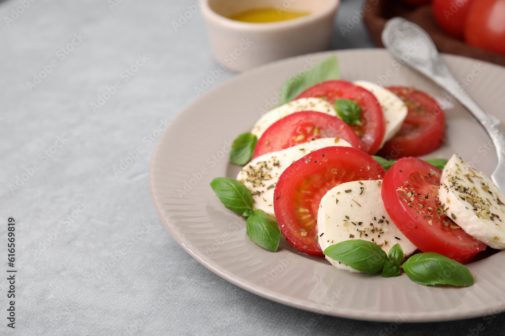 Delicious Caprese salad with tomatoes, mozzarella, basil and spices on light grey table, closeup Delicious Caprese salad with tomatoes, mozzarella, basil and spices on light grey table, closeup