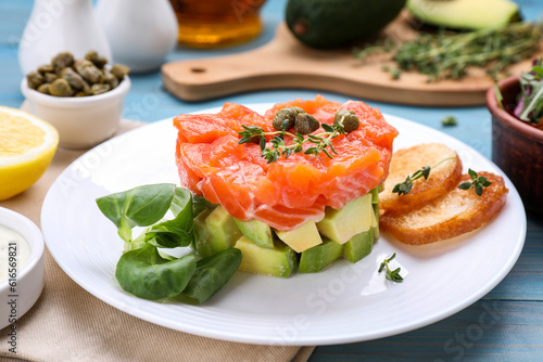 Delicious salmon tartare served with avocado and croutons on light blue table  closeup