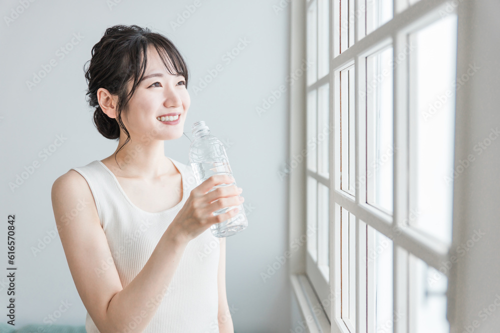 家でペットボトルの水・ミネラルウォーター・白湯を飲むリラックスした女性
