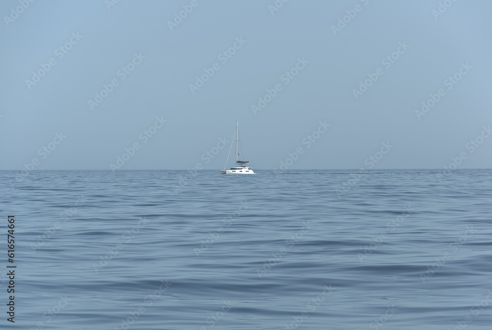 A serene image with a blue sky, sparkling sea, and a majestic sailboat sailing gracefully amidst the vastness. 