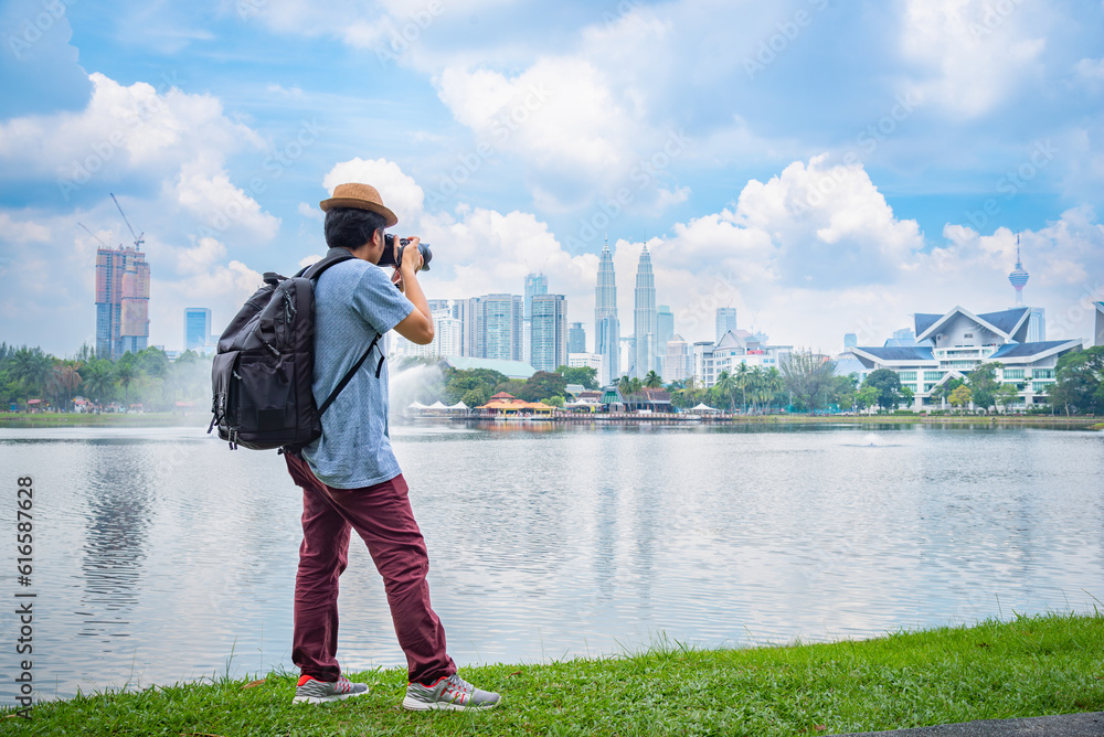 Obraz premium Photographer or Traveller using a professional DSLR camera take photo beautiful landscape of Kuala Lumpur skyscraper at Titiwangsa park Kualalumpur city, Malaysia.