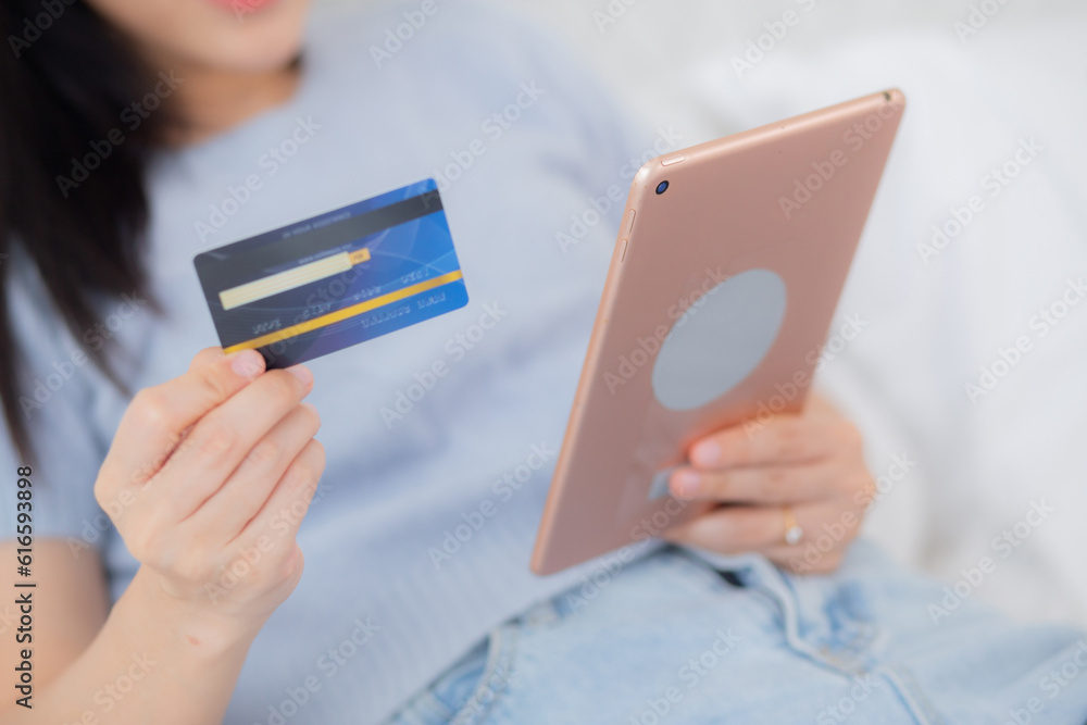 Closeup hands young woman sitting on bed using digital tablet shopping online with credit card in the bedroom at home, female paying with transaction financial, purchase and payment, business concept. Closeup hands young woman sitting on bed using digital tablet shopping online with credit card in the bedroom at home, female paying with transaction financial, purchase and payment, business concept.