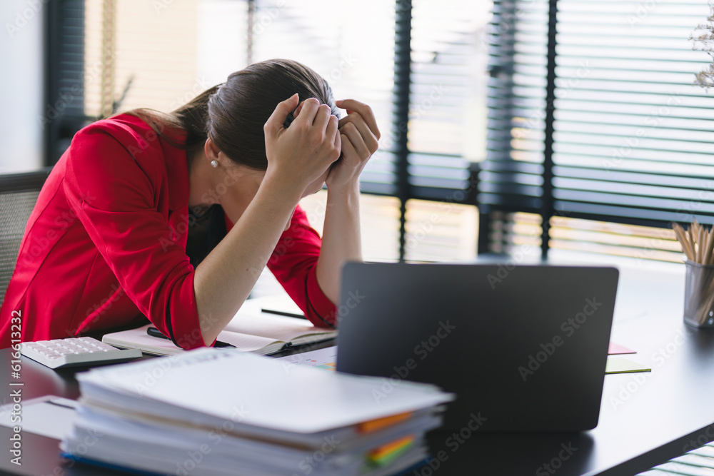 The stressed and exhausted millennial businesswoman is seen sitting at her office desk with her hand on her head, indicating a hard working day where she is overloaded with work. The stressed and exhausted millennial businesswoman is seen sitting at her office desk with her hand on her head, indicating a hard working day where she is overloaded with work.