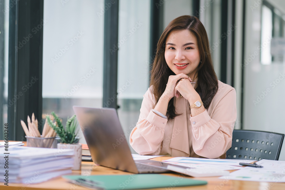 A portrait of a smiling, young, beautiful, professional, and confident millennial Asian businesswoman using a digital tablet to analyze sales data at a modern office.