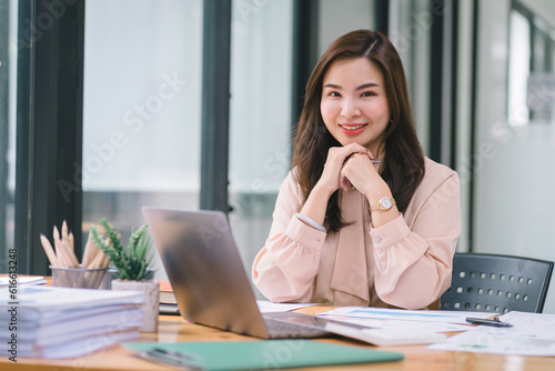 A portrait of a smiling, young, beautiful, professional, and confident millennial Asian businesswoman using a digital tablet to analyze sales data at a modern office.