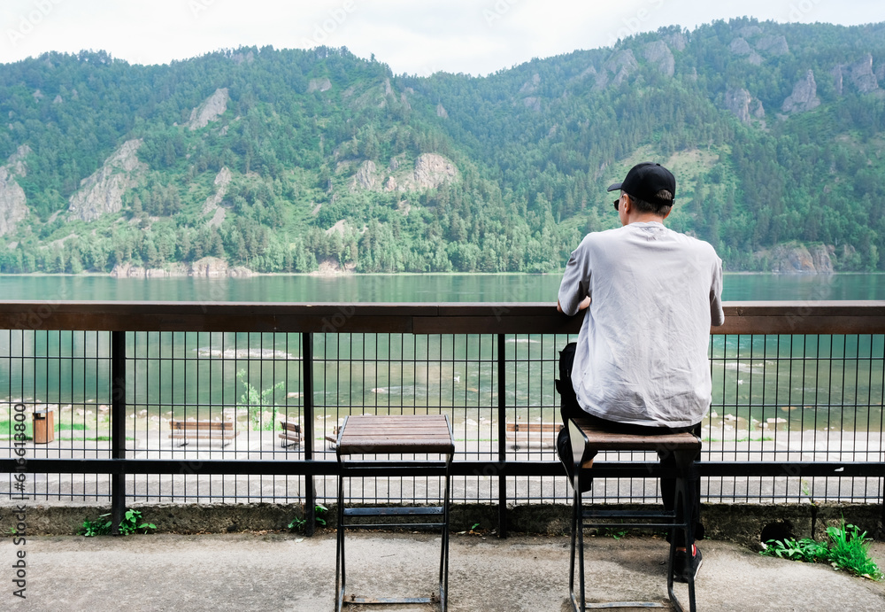 Back view of male traveler sitting on wooden bench while enjoying amazing nature in mountains. Man drinking coffee outdoor in morning. Back view of male traveler sitting on wooden bench while enjoying amazing nature in mountains. Man drinking coffee outdoor in morning.