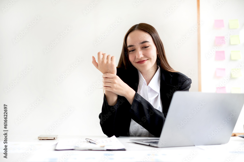 An Asian woman is sitting overtime with her laptop and her wrist aches while working at the office An Asian woman is sitting overtime with her laptop and her wrist aches while working at the office