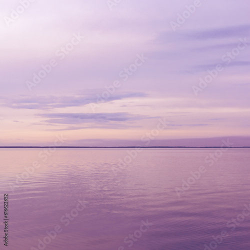 Colorful sky background on sunset or sunrise, purple pastel color clouds and surface water on lake Ik. Nature abstract composition with reflections on water, natural blue purple shades of skyline