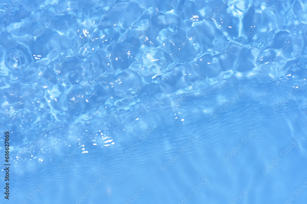 Obraz premium Blue water with ripples on the surface. Defocus blurred transparent blue colored clear calm water surface texture with splashes and bubbles. Water waves with shining pattern texture background.