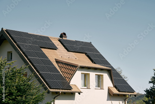 Solar panels on the roof of the modern house. Residential house cottage with blue shiny solar photo voltaic panels system on roof. Renewable ecological green energy production concept. Sustainable.