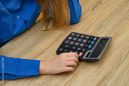Zapracowana kobieta przy biurku, liczy na kalkulatorze