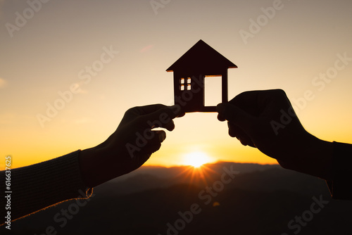 Photographie silhouette of male and female hands holding model house at sunset Concept of buying houses, real estate