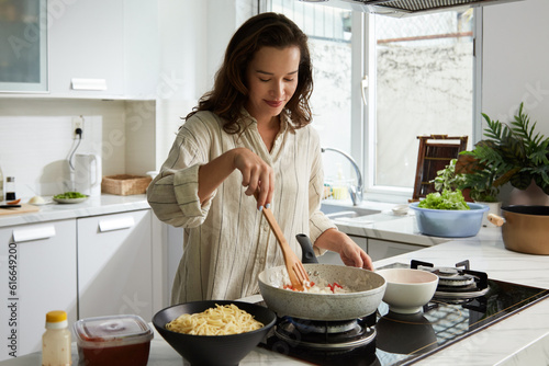 Fotótapéta Smiling woman stirring vegetables in frying pan when cooking dinner