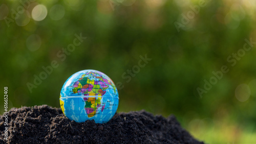 The small globe, earth is on hand, grass, leaf. The globe has maps on it and environmental map. The earth map shown geography continents, countries. The globe ball is the symbol of our planet earth.