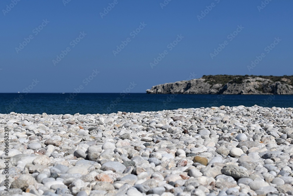 Pebble beach of the Greek island of Rhodes with blue sea and rocky mountains in the background
