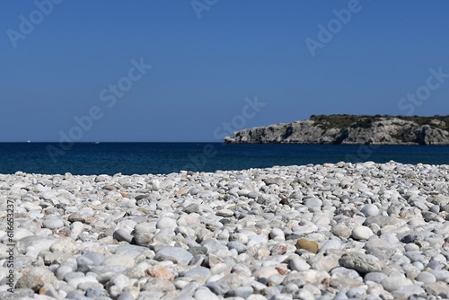 Pebble beach of the Greek island of Rhodes with blue sea and rocky mountains in the background
