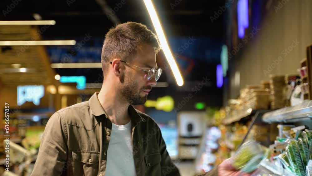 Young man shopping in grocery store. Side view of focused man holding shopping baskets and choosing fresh vegetables in supermarket. Shopping concept Young man shopping in grocery store. Side view of focused man holding shopping baskets and choosing fresh vegetables in supermarket. Shopping concept