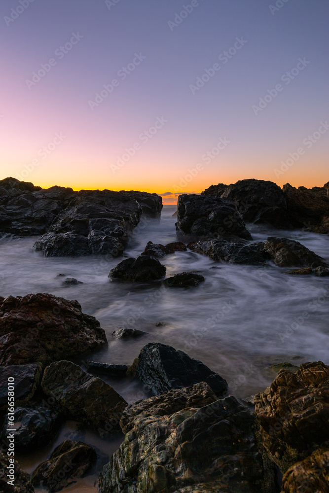 Long exposure rocky seascape view with sunrise glow.
