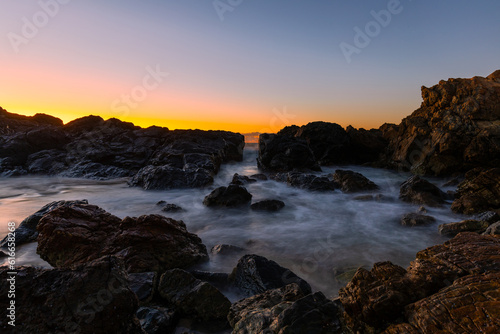 Long exposure rocky seascape view with sunrise glow.