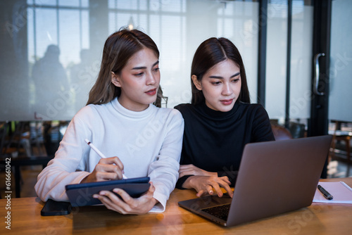 Two cheerful young Asian female college students working on the school project using laptop computers and tablets together in private study room