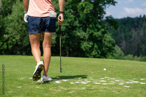 Beautiful tanned legs of a golfer girl on the golf course. Girl player with golf clubs on the lawn prepares to hit. Sports and summer hobbies.
