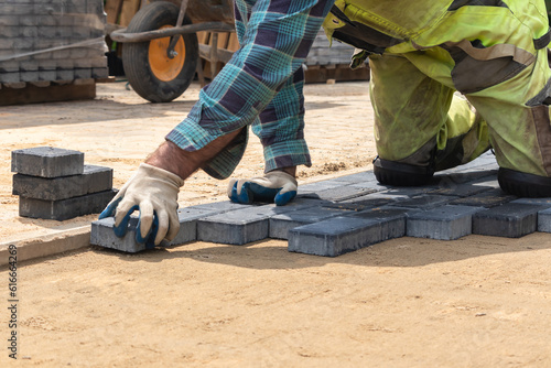 A worker laying paving stones at a sidewalk construction site, close up Pracownik układający kostkę brukową na placu budowy chodnika, z bliska