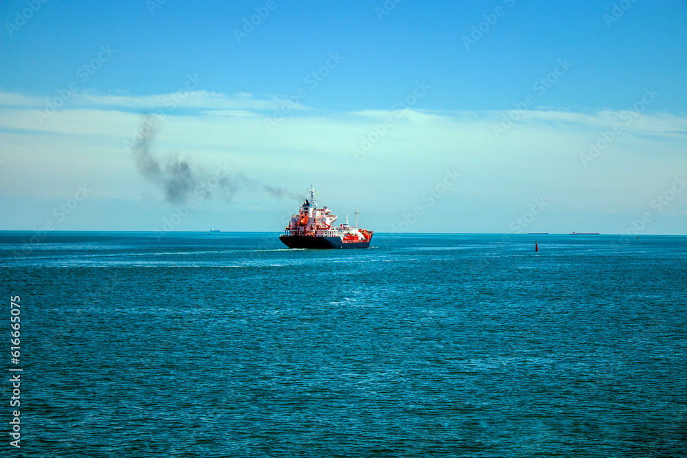 A large beautiful ship with a large number of containers floats on the horizon in the azure sea and releases smoke from the chimney A large beautiful ship with a large number of containers floats on the horizon in the azure sea and releases smoke from the chimney