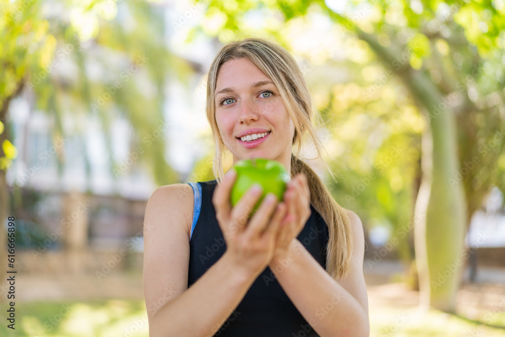 Young blonde woman at outdoors holding an apple with happy expression Young blonde woman at outdoors holding an apple with happy expression