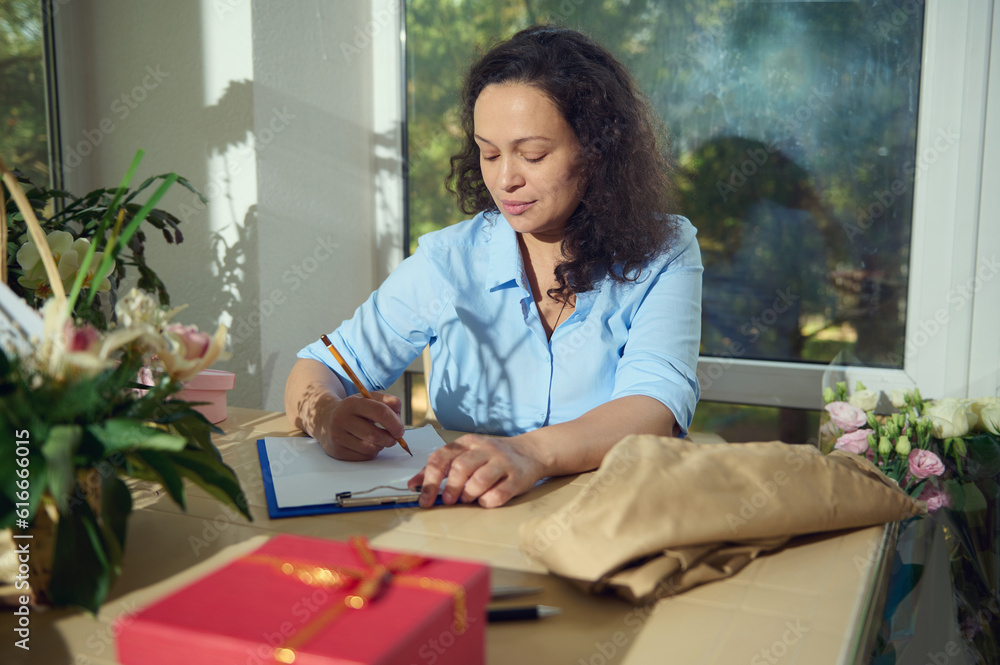 Portrait of a pregnant African American woman, business owner working at floral shop, receiving order, writing down notes on a paper sheet. People. Hobby. Startup. Small business cocnept Portrait of a pregnant African American woman, business owner working at floral shop, receiving order, writing down notes on a paper sheet. People. Hobby. Startup. Small business cocnept