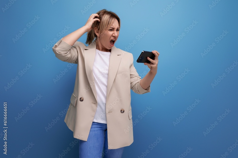 doubtful business woman in a jacket with blond hair holding a credit card on a studio background with copy space doubtful business woman in a jacket with blond hair holding a credit card on a studio background with copy space