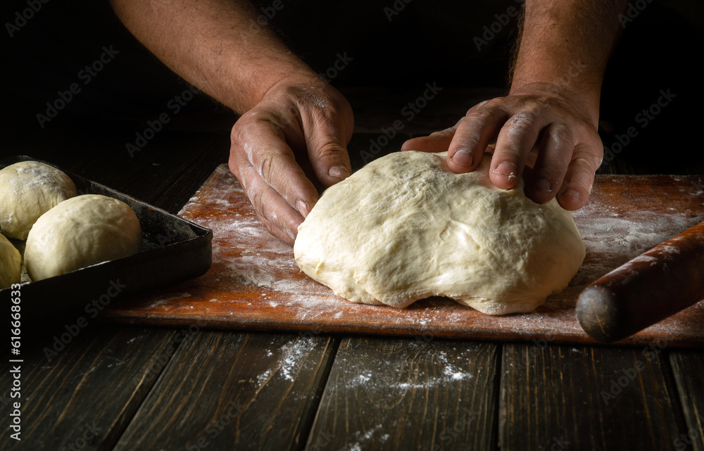Close-up of a male baker's hands kneading dough on a kitchen board with flour powder. The concept of baking and confectionery.