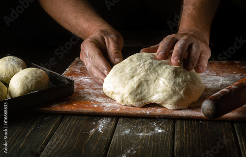 Close-up of a male baker's hands kneading dough on a kitchen board with flour powder. The concept of baking and confectionery.