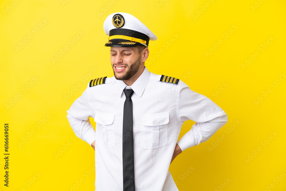 Airplane caucasian pilot isolated on yellow background suffering from backache for having made an effort Airplane caucasian pilot isolated on yellow background suffering from backache for having made an effort