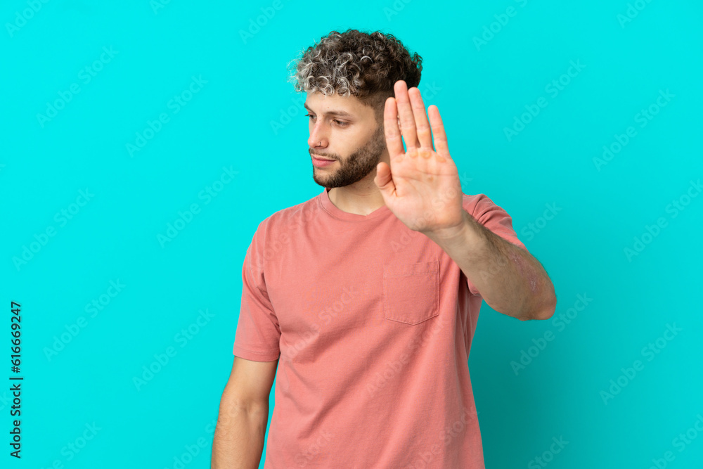 Naklejka premium Young handsome caucasian man isolated on blue background making stop gesture and disappointed