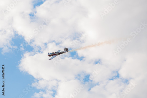 Fototapeta Naklejka Na Ścianę i Meble -  Small retro airplane, light aircraft flying in blue cloudy sky and doing stunts at Air Show. Performance, extreme, aerobatic and sport concept