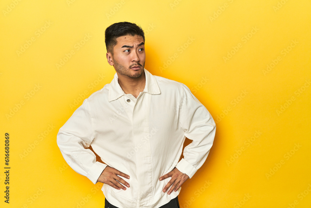 Asian man in crisp white shirt on yellow studio confused, feels doubtful and unsure. Asian man in crisp white shirt on yellow studio confused, feels doubtful and unsure.