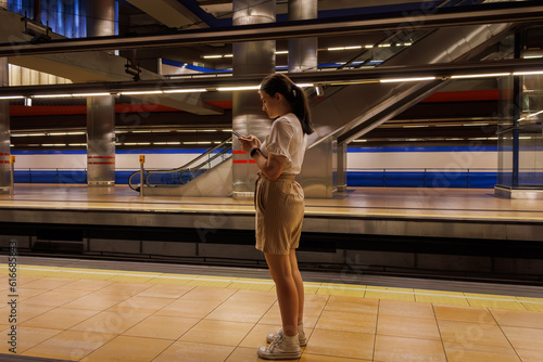 teenage girl in shorts looking at her cell phone in the subway station to know her destination